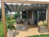 Grey roman blind canopy installed on a wooden pergola over a terrace with outdoor wicker furniture and plants