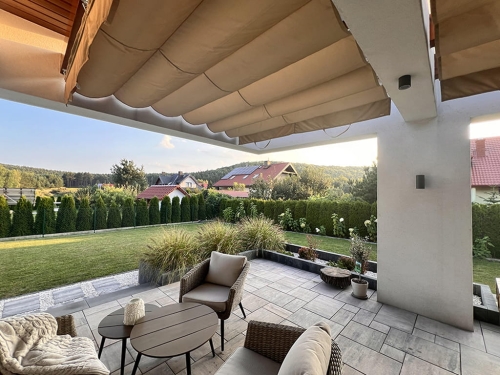 Retractable terrace roman blind providing shade over a modern patio with comfortable lounge furniture and garden view