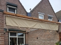 Estor plegable de terraza Premium beige 3x5 m montado sobre una viga de madera en una pared de ladrillo