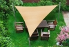 Beige triangular HDPE sun shade sail over a wooden garden dining set in a lush green backyard.