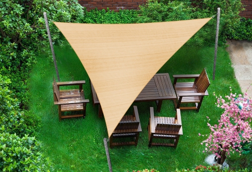 Beige triangular HDPE sun shade sail over a wooden garden dining set in a lush green backyard.