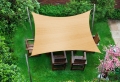Zandkleurig rechthoekig schaduwdoek 5x6 m in de tuin boven houten stoelen en tafel op het gazon
