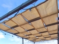 Beige solskyddsvåd för paviljong av HDPE-tyg monterad under ett pergolatak med en ljusslinga.