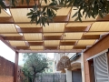 Sandfarbenes HDPE-Sonnensegel für Pavillons, montiert an einer Holz-Terrassenpergola mit geflochtenen Lampen