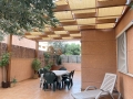 Beigefarbene HDPE-Sonnenschutzlamelle an einer Holzpergola über der Terrasse mit Gartenmöbeln montiert