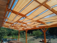 Zandkleurige HDPE lamellen zonnedoek 0,5x5 m gemonteerd onder terrasoverkapping beschermt tegen zon en biedt schaduw