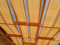 Beige HDPE sunshade fabric strip installed on a wooden pergola structure for patio shade under a blue sky