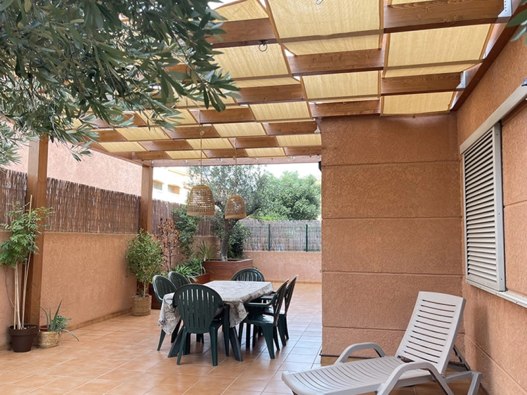 Outdoor patio with beige HDPE sun shade panels on a wooden pergola over an outdoor dining set and lounge chair.