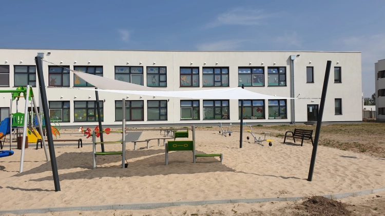 Maßgefertigtes weißes Sonnensegel beschattet einen modernen Kindergarten-Spielplatz auf sandigem Untergrund
