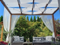 Custom white sunshade sails woven through a wooden pergola over a garden lounge set with grey cushions and white curtains