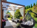 Vit solskyddslängd för altan monterad på en träpergola över en terrass med utemöbler