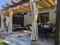 Beige waterdicht tuingordijn op maat gemonteerd op een houten terraspergola met loungemeubels