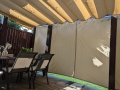 Beige waterdicht tuingordijn op maat gemonteerd op een terras met pergola en tuinmeubelen