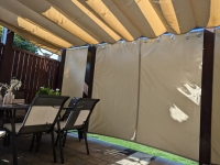 Beiger wasserdichter Gartenvorhang nach Maß, montiert auf einer Terrasse mit Pergola und Loungemöbeln