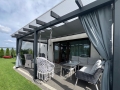 Vela de sombra gris impermeable a medida instalada bajo el techo de la terraza con muebles de jardín y columpio