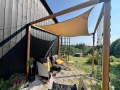Beige waterproof sun shade sail mounted on a wooden pergola over an outdoor lounge sofa with cushions