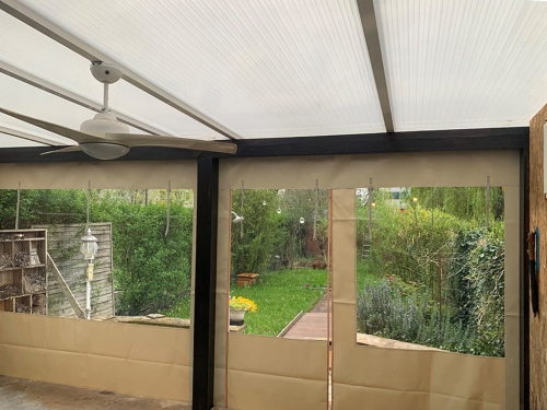 Priehľadná plachta na terasu s béžovým okrajom a oknom, namontovaná pod zastrešením s ventilátorom