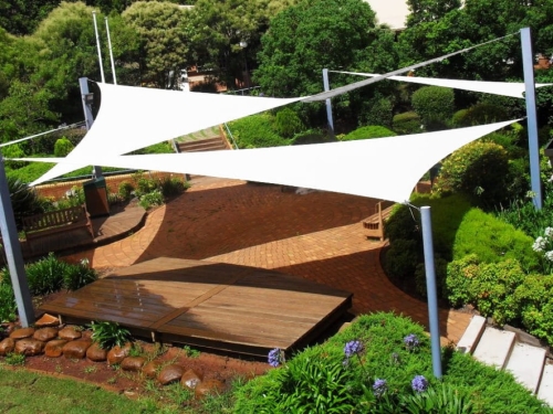 Custom white triangular sun shade sails over a brick patio with garden furniture and lush landscaping.