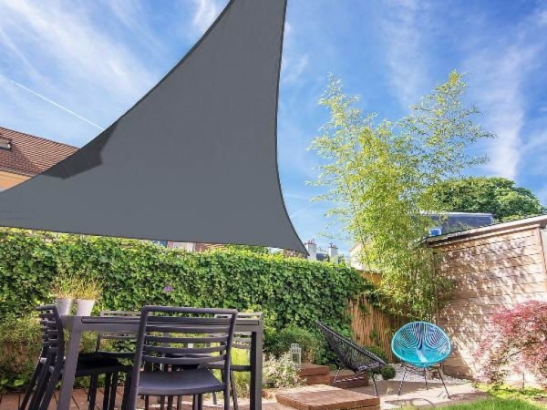 Grey triangular waterproof sail shade installed over a modern outdoor dining set in a garden with bamboo and ivy.