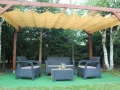 Beige retractable HDPE Roman blind canopy over dark wicker garden furniture set on a green patio surface outdoors