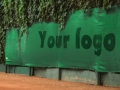 Custom green tennis court windbreak screen with dark logo placement, mounted on a fence background.