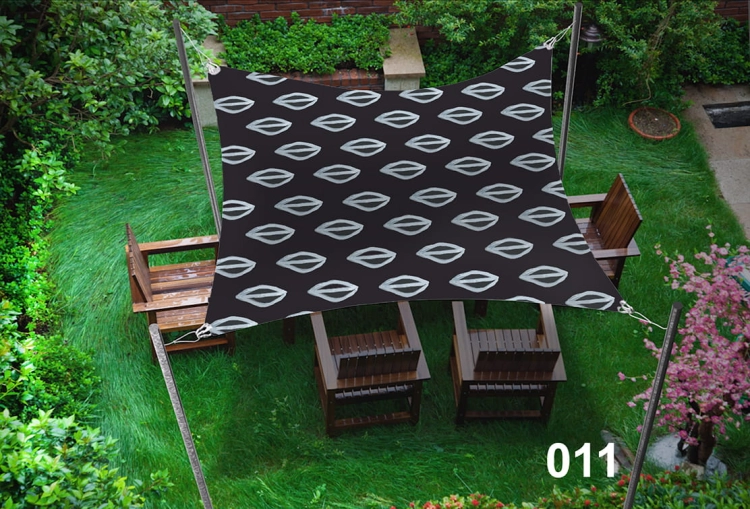 Dunkelbraunes Sonnensegel mit weißem Muster, das Gartenmöbel auf dem Rasen beschattet.