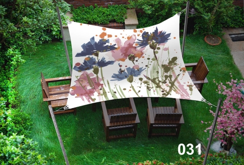 Sun shade sail with a floral print over a wooden outdoor seating area in a green garden.