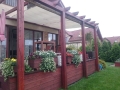 Weißes Sonnensegel an einer Holzpergola über einer Terrasse mit Blumen in Töpfen montiert