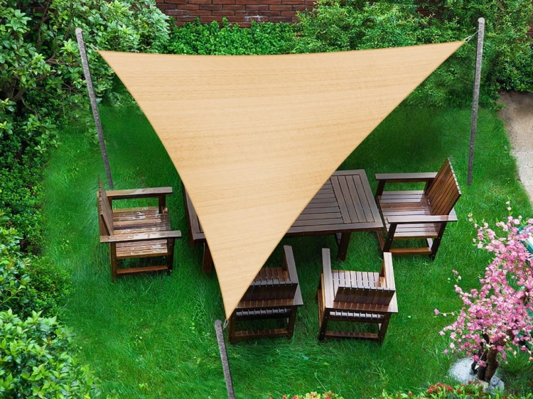Dreieckiges beiges Sonnensegel HDPE 3x3x4,2 m über einem Gartenmöbel-Set aus Holz auf dem Rasen