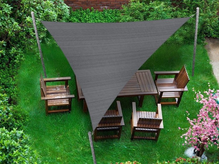 Grey triangular shade sail made of HDPE fabric over a wooden garden furniture set on a green lawn.