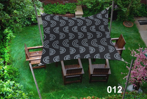 Waterproof shade sail with a black and white rainbow pattern over four wooden chairs in a lush garden.