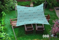 Waterproof sun shade sail with a blue whale pattern over outdoor wooden patio furniture in a green garden.