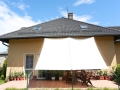 Vela ombreggiante scorrevole bianca impermeabile installata su una terrazza con mobili da giardino e piante in vaso