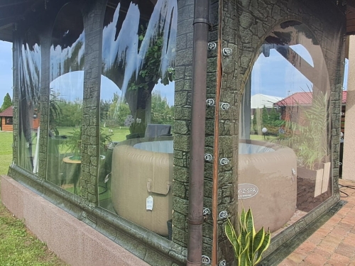 Transparent custom terrace tarp with arched windows and faux stone print enclosing an inflatable hot tub and furniture