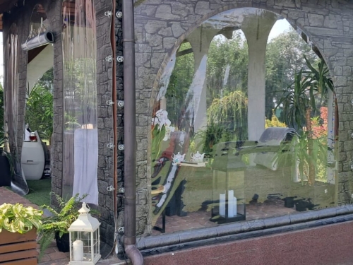 Custom transparent patio tarp with printed stone pattern and arched window overlooking a garden lounge area