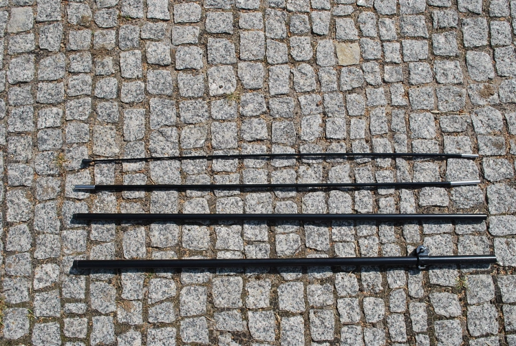 Four black fiberglass and aluminum pole segments for an outdoor custom beach flag displayed on a cobblestone surface