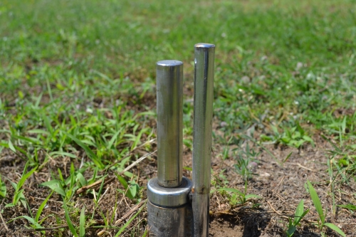 Metal ground spike rotator for an outdoor beach flag banner installed in a grassy area.