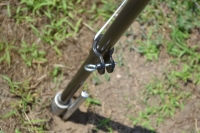 Black outdoor beach flag pole base secured into the ground with a metal spike and adjustment screw.