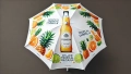White patio umbrella with tropical fruit graphics and a chilled beverage bottle design on a white canopy