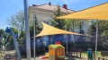Gelbe Sonnensegel auf einem Spielplatz, montiert an Stahlpfosten über einem kleinen Spielhaus mit Rutsche