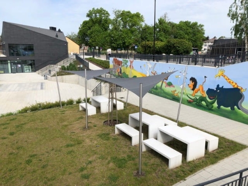 Grijze schaduwdoeken op maat boven witte tafels en banken op een moderne speeltuin.