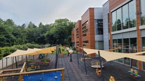 Beige shade sails over a modern school playground with outdoor equipment and UV-resistant sun protection canopy.