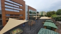 Beige shade sails over a school playground with play equipment and wooden tables for UV protection.