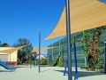 Světle stínicí plachty na míru namontované nad moderním dětským hřištěm s houpačkami a skluzavkou