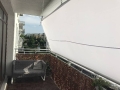 Weißes wasserdichtes Premium-Sonnensegel auf einem Balkon über einem grauen Sofa und einer braunen Geländerverkleidung montiert