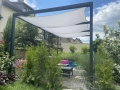 Wasserdichtes Sonnensegel an einer dunklen Pergola-Konstruktion in praller Sonne über einer Terrasse mit Möbeln