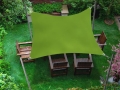 Grünes Premium Sonnensegel über einem Holzmöbel-Set auf dem Rasen im Garten