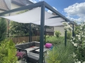 Wasserdichtes Premium Sonnensegel auf einer schwarzen Pergola über Gartenmöbeln im Grünen