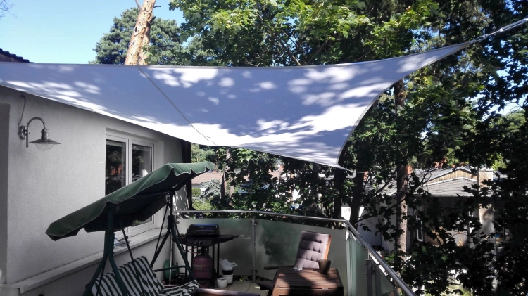 Large triangular waterproof sun shade sail installed over a residential balcony with outdoor furniture and a grill