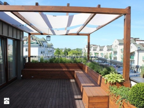 White sunshade sail fabric strips installed on a wooden rooftop pergola with deck seating and built-in planters